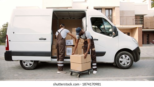 Young handsome Caucasian delivery man giving boxes from van to African American man colleague standing on street and putting them on cart. delivering shipment. Male post office workers Courier concept - Powered by Shutterstock