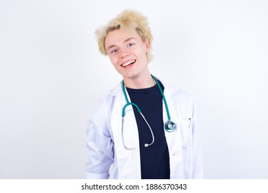 Young Handsome Caucasian Doctor Man Standing Against White Studio Wall With Broad Smile, Shows White Teeth, Feeling Confident Rejoices Having Day Off.