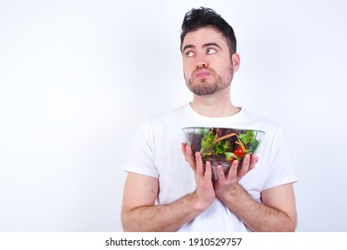 Young Handsome Caucasian Man Holding A Salad Bowl Against White Background Sending Blow Kiss With Pout Lips And Holding Palms To Send Air Kiss.