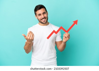 Young handsome caucasian man isolated on blue background holding a catching a rising arrow and doing coming gesture - Shutterstock ID 2103392507