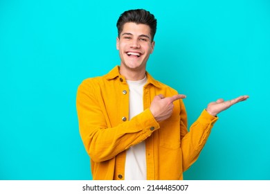 Young handsome caucasian man isolated on blue bakcground holding copyspace imaginary on the palm to insert an ad - Shutterstock ID 2144485007