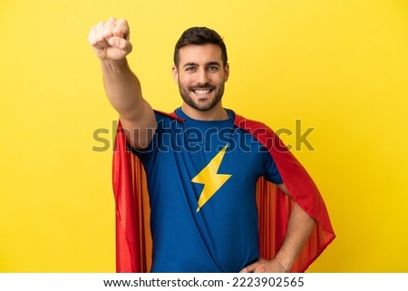 Young handsome caucasian man isolated on yellow background in superhero costume with proud gesture