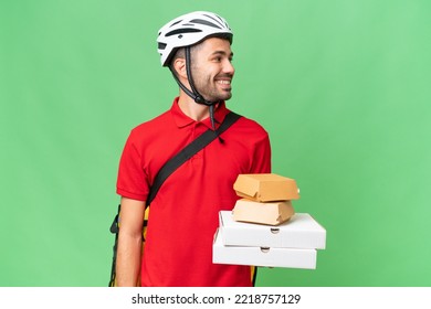 Young Handsome Caucasian Man With Thermal Backpack And Holding Takeaway Food Over Isolated Background Looking Side