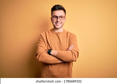 Young Handsome Caucasian Man Wearing Glasses And Casual Winter Sweater Over Yellow Background Happy Face Smiling With Crossed Arms Looking At The Camera. Positive Person.