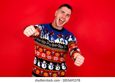 Young Handsome Caucasian Man Wearing Christmas Sweater Against Red Wall, Imagine Steering Wheel Helm Rudder Passing Driving Exam Good Mood Fast Speed