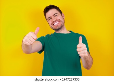  young handsome caucasian man wearing green t-shirt against yellow background approving doing positive gesture with hand, thumbs up smiling and happy for success. Winner gesture. - Powered by Shutterstock