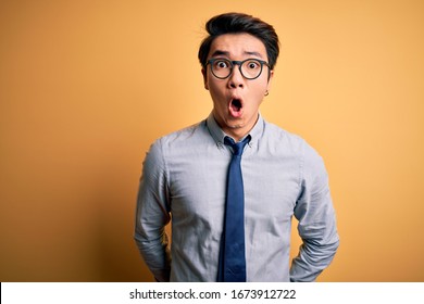 Young Handsome Chinese Businessman Wearing Glasses And Tie Over Yellow Background Afraid And Shocked With Surprise Expression, Fear And Excited Face.