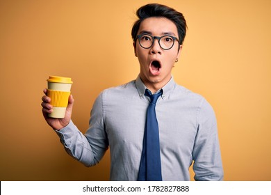 Young Handsome Chinese Man Drinking Glass Of Take Away Coffee Over Yellow Background Scared In Shock With A Surprise Face, Afraid And Excited With Fear Expression