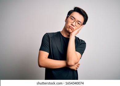 Young Handsome Chinese Man Wearing Black T-shirt And Glasses Over White Background Thinking Looking Tired And Bored With Depression Problems With Crossed Arms.