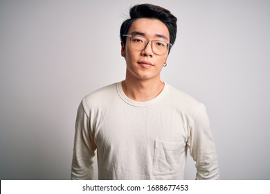 Young Handsome Chinese Man Wearing Casual T-shirt And Glasses Over White Background With Serious Expression On Face. Simple And Natural Looking At The Camera.