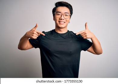 Young Handsome Chinese Man Wearing Black T-shirt And Glasses Over White Background Looking Confident With Smile On Face, Pointing Oneself With Fingers Proud And Happy.