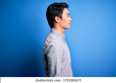 Young Handsome Chinese Man Wearing Casual Shirt Standing Over Isolated Blue Background Looking To Side, Relax Profile Pose With Natural Face And Confident Smile.
