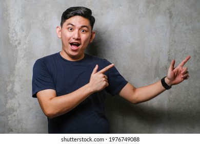 Young Handsome Chinese Man Wearing Navy Tshirt Smiling And Looking At The Camera Pointing With Two Hands And Fingers To The Side Over Concrete Wall Background