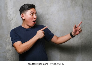 Young Handsome Chinese Man Wearing Navy Tshirt Smiling And Looking At The Camera Pointing With Two Hands And Fingers To The Side Over Concrete Wall Background