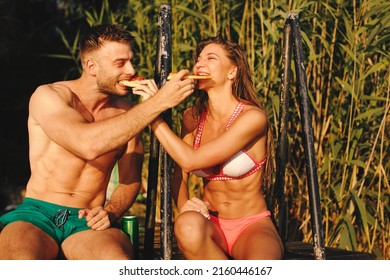 Young Handsome Couple Eating Pizza On The Dock By The Lake