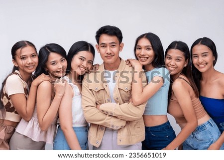 A young handsome and dapper asian guy in the center together with 6 attractive ladies. 7 college students posing against a white backdrop.