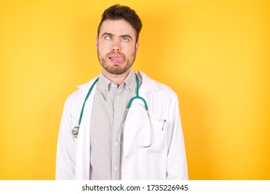 Young Handsome Doctor Man, Making Grimace Face Crossing Her Eyes And Showing Tongue Isolated Over White Background. Being Funny And Crazy