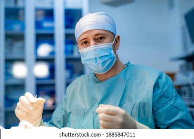 Young handsome doctor is operating patient in modern clinic. Male surgeon in scrubs and mask.