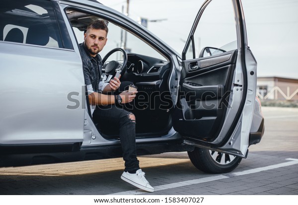 Young handsome driver man with smartphone\
serfing internet and drink black\
coffee
