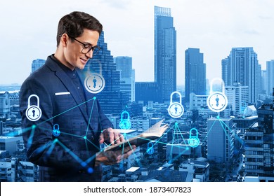 A young handsome eastern cybersecurity developer explores his notes from day planner to protect clients confidential information. IT lock icons over Bangkok city background.