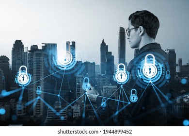 A young handsome eastern cybersecurity developer explores new approaches to protect clients confidential information using phone. IT lock icons over Bangkok city background.