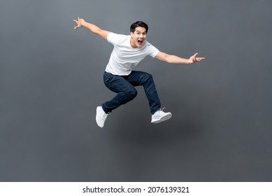 Young handsome energetic Asian man jumping with hands outstratched in isolated studio gray background - Shutterstock ID 2076139321