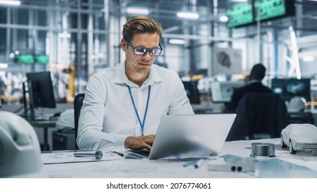 Young Handsome Engineer Working and Managing Projects on Laptop Computer in an Office at Car Assembly Plant. Industrial Specialist Working on Vehicle Parts in Technological Development Facility.