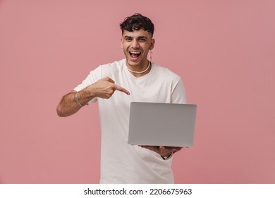 Young Handsome Enthusiastic Man With Opened Mouth Holding Laptop And Pointing On It, While Standing Over Pink Isolated Background