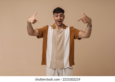 Young Handsome Enthusiastic Man With Opened Mouth Pointing And Looking On Copyspace In Front Of Him , While Standing Over Isolated Brown Background