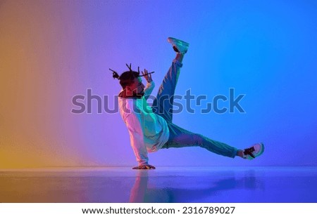 Young handsome guy in casual clothes and dreads dancing breakdance against gradient multicolored studio background in neon light. Concept of street style dance, fashion, youth, hobby, dynamics, ad