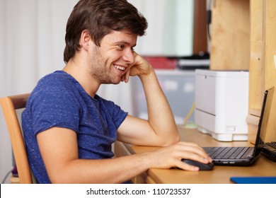 Young handsome guy with laptop next to table in room, background