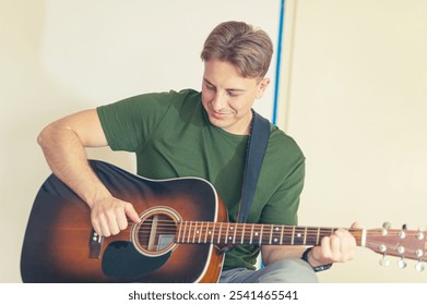 A young handsome guy is practicing playing an acoustic guitar