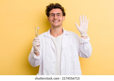 Young Handsome Guy Smiling Happily, Waving Hand, Welcoming And Greeting You. Dentist Concept