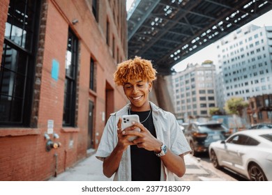 Young handsome guy walks across the street, typing messages on a smartphone and smiling - Powered by Shutterstock