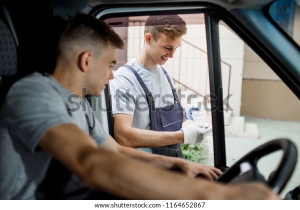 A young handsome guy wearing\
uniform is looking out of the car window. Another worker wearing\
uniform is holding the clipboard. House move, mover\
service.