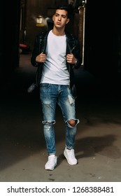 young, handsome guy in a white T-shirt, black, leather jacket and blue, torn jeans is on the street, model, city walk, live style.in white sneakers
