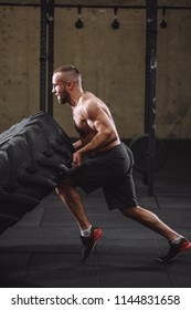 Young Handsome Healthy Man With Tensed Face Performing Exercise With Tractor Tire. Side View Full Length Photo