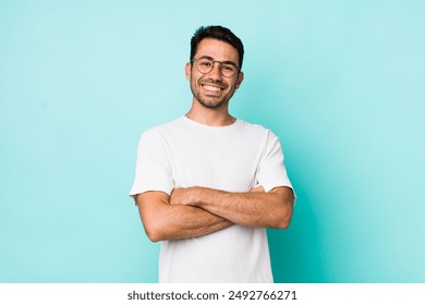 young handsome hicpanic man laughing happily with arms crossed, with a relaxed, positive and satisfied pose