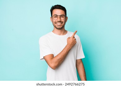 young handsome hicpanic man smiling cheerfully, feeling happy and pointing to the side and upwards, showing object in copy space - Powered by Shutterstock