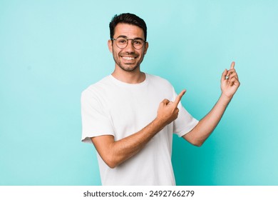 young handsome hicpanic man smiling happily and pointing to side and upwards with both hands showing object in copy space - Powered by Shutterstock