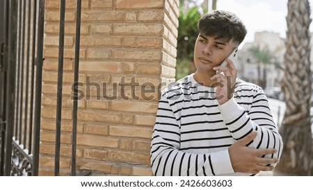 Young, handsome hispanic man engrossed in a serious phone conversation on a city street, his cool, casual lifestyle personified in every relaxed, concentrated expression.