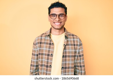 Young handsome hispanic man wearing casual clothes and glasses looking positive and happy standing and smiling with a confident smile showing teeth 