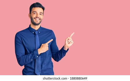Young handsome hispanic man wearing business clothes smiling and looking at the camera pointing with two hands and fingers to the side.  - Shutterstock ID 1880880649