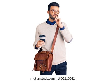 Young handsome hispanic man wearing leather bag and drinking take away coffee serious face thinking about question with hand on chin, thoughtful about confusing idea 