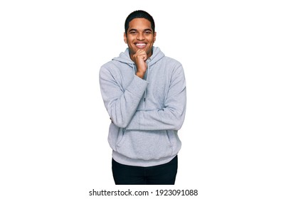 Young handsome hispanic man wearing casual sweatshirt looking confident at the camera with smile with crossed arms and hand raised on chin. thinking positive. 