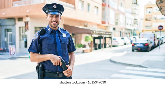 Young Handsome Hispanic Policeman Wearing Police Uniform Smiling Happy. Standing With Smile On Face Holding Shotgun At Town Street.