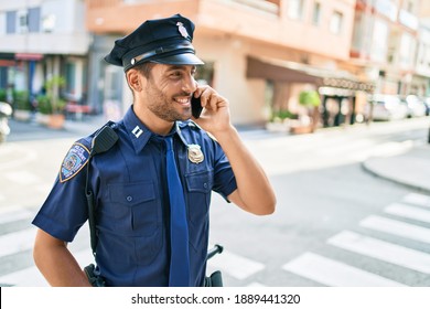 Young Handsome Hispanic Policeman Wearing Police Uniform Smiling Happy. Standing With Smile On Face Having Conversation Talking On The Smartphone At Town Street.