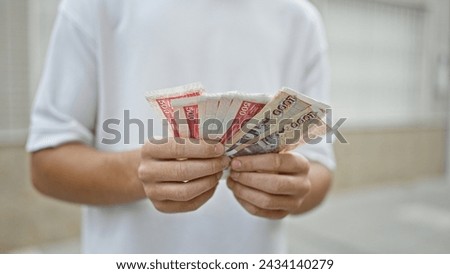 Young handsome hispanic teenager counting stack of iceland krona banknotes on an urban street, exploring finance and investment