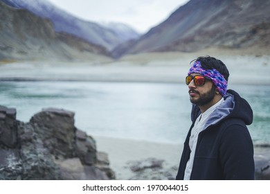 Young handsome indian male with trekking gears posing in front of a camera with mountains and river in background.