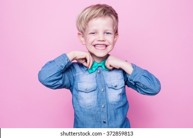 Young Handsome Kid Smiling With Blue Shirt And Butterfly Tie. Studio Portrait Over Pink Background